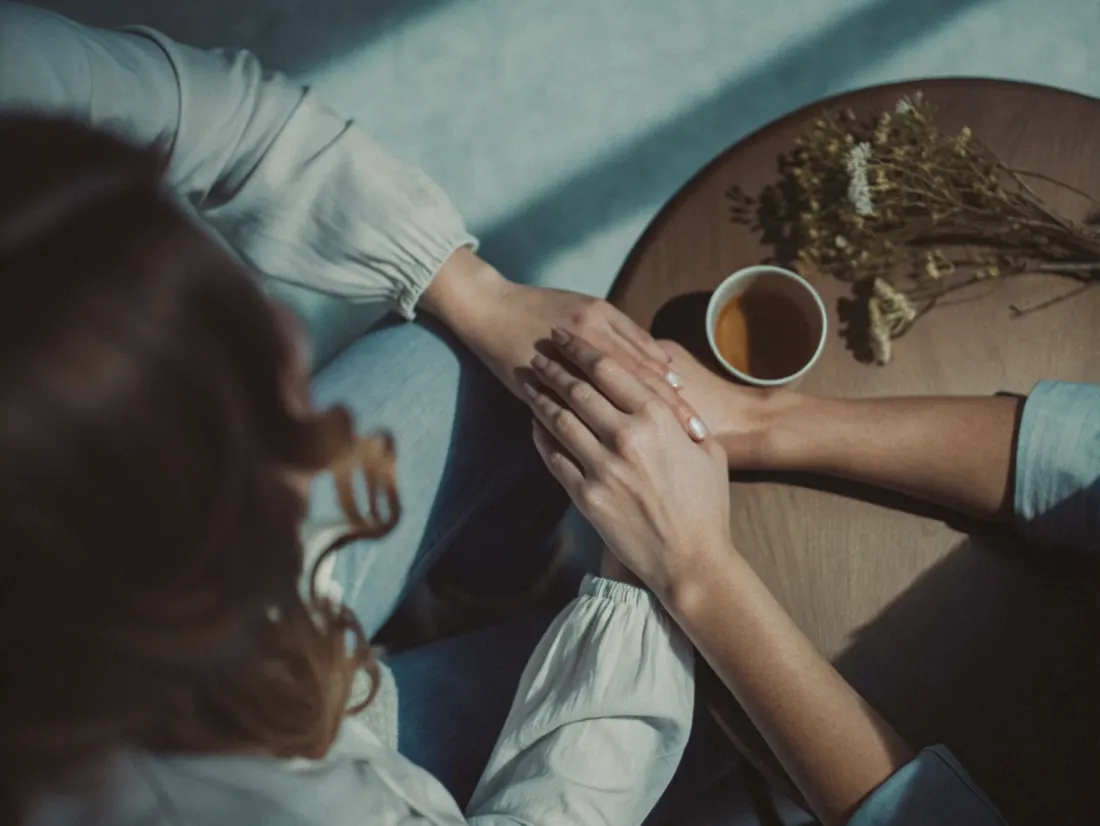 Duas mulheres numa sala serena, uma a ouvir a outra com atenção, à luz quente de um candeeiro