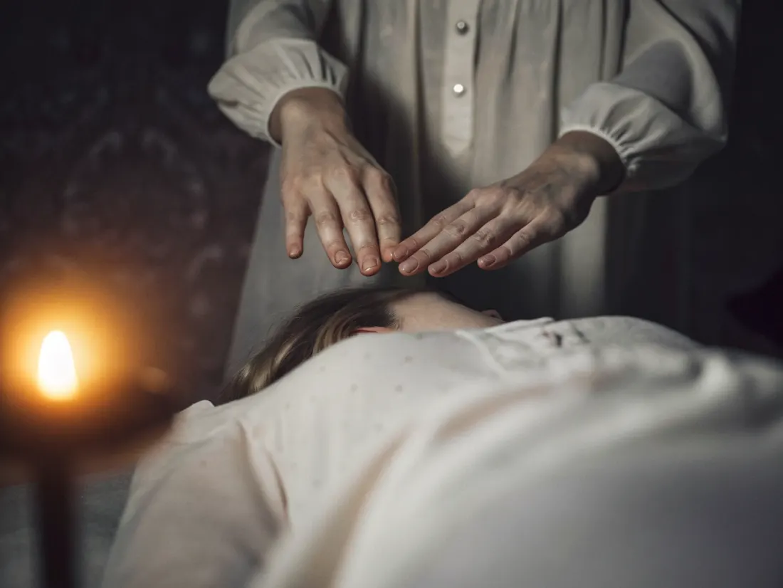 Mãos de uma terapeuta suspensas sobre as costas de uma pessoa deitada, com uma luz dourada suave, numa sessão de Reiki