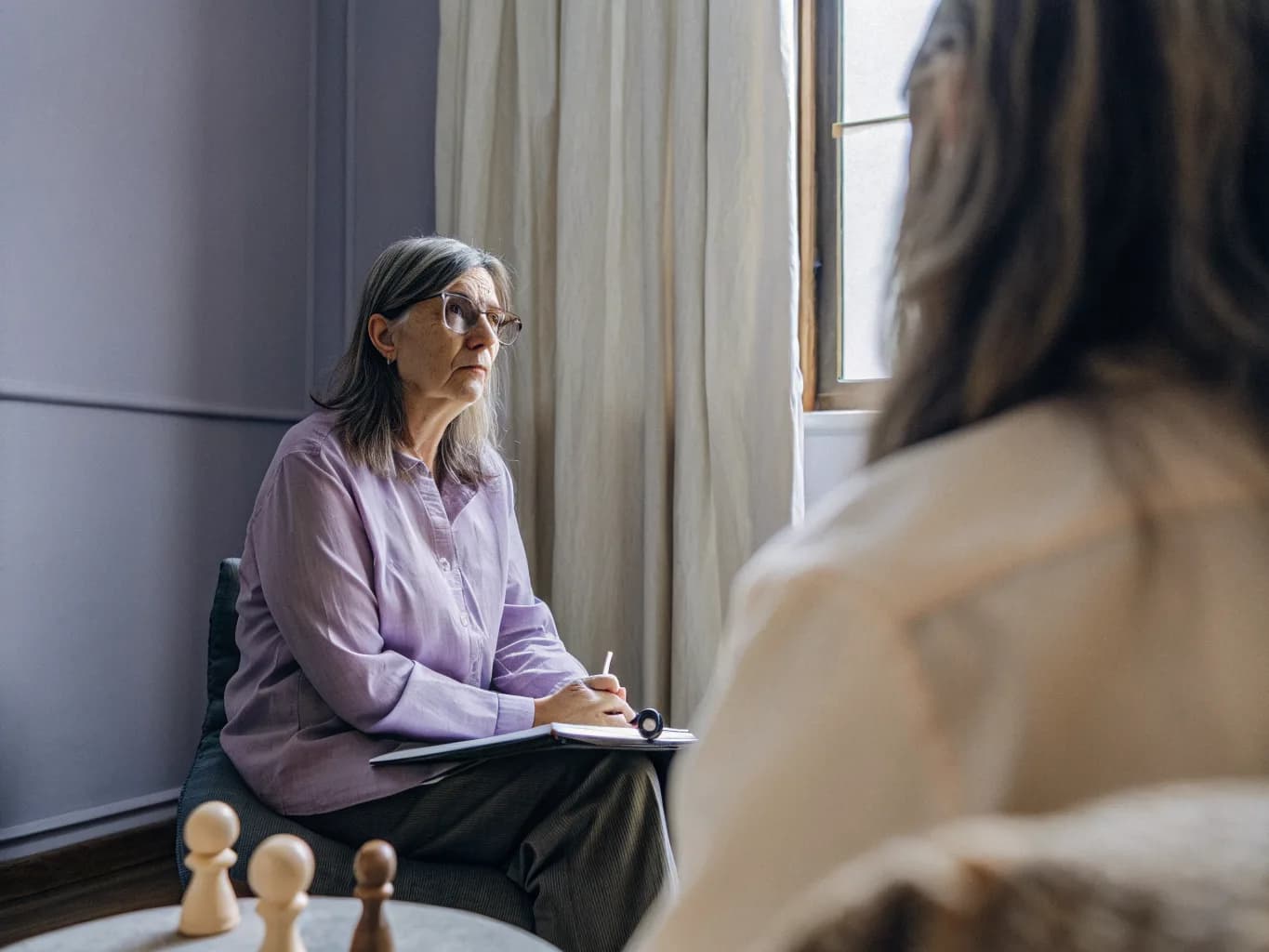Terapeuta a escutar uma cliente numa sala de consulta clara, com figuras de madeira na mesa