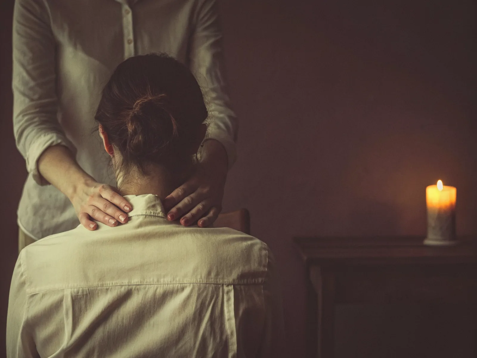 As mãos de uma terapeuta pousadas nos ombros de uma pessoa sentada, com uma luz dourada suave entre as mãos e os ombros